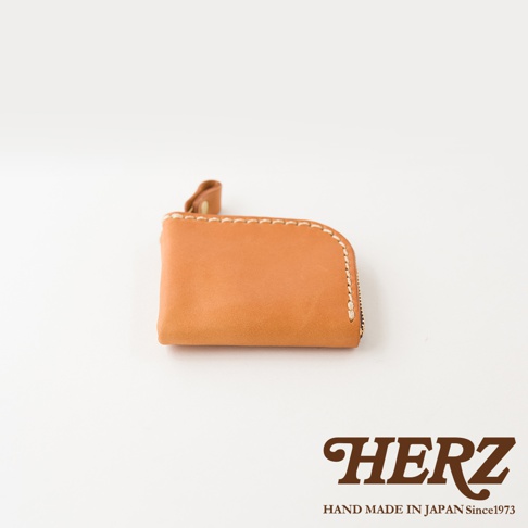 日本HERZ職人手作皮革零錢包，選用棕色Stare皮革製成，正面呈現簡約的正方形輪廓並帶有圓角設計，邊緣以粗縫線手工縫製，側面飾有拉鍊開口與皮質拉環，下方印有HERZ品牌標誌與產地說明。