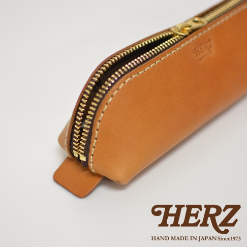 職人手作皮革三角收納筆袋，採用天然皮革材質，呈現溫潤的棕褐色調，搭配金色拉鍊與縫線，簡約而精緻。