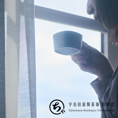 一位女性站在明亮的窗邊，手持一只簡約質感的白色美濃燒馬克杯準備飲用，畫面下方印有宇治田原製茶場直賣部的品牌識別標誌。