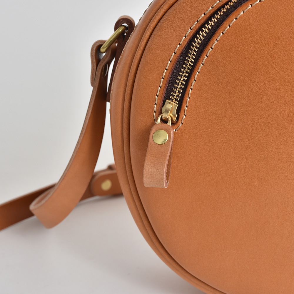 職人手作皮革小圓包，採用經典棕褐色皮革，搭配黃銅色拉鍊與五金配件，設計簡約實用。