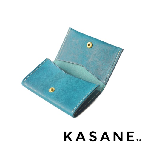 KASANE TH 品牌藍綠色皮革卡夾，帶有金色按鈕，置於白色背景上