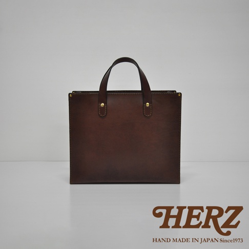 深棕色皮革直式托特包，具有兩個短提把，以鉚釘固定於包身頂部，整體為簡潔方形設計，材質為皮革。