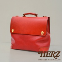 紅色皮革製成的波士頓包，頂部有提把，正面有金色旋轉鎖扣，包包底部有加固的皮革飾片。