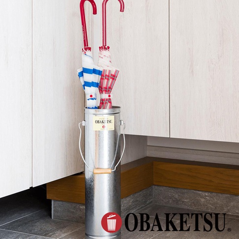 OBAKETSU 銀色手工製傘桶，內有兩把藍白條紋及紅格紋的傘，傘桶上有 OBAKETSU 品牌標誌。