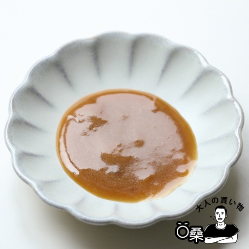 一個帶有灰藍色邊緣的白色花邊小碟子，盛著一碟濃稠的淺棕色芝麻沾醬，醬料表面有光澤。