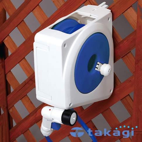 白色壁掛式自動收捲水管架，配有藍色水管和噴嘴，安裝在木製栅欄上。