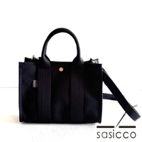 黑色三河木綿刺子織方形托特包，帶有提把及可拆卸斜背帶，包身織紋明顯，中間有圓形金屬品牌標誌。