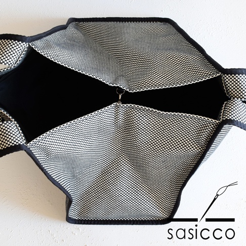 展開狀態的三河木綿刺子織托特包，外層為黑白格紋布料，內裡為黑色，包身邊緣有黑色滾邊，中間有一個金屬扣環。