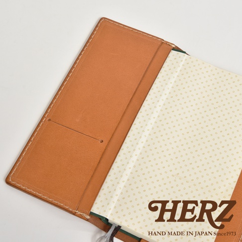 職人手作皮革旅行記事本書套，採用淺棕色皮革，內有兩個卡槽，搭配印有「HERZ」字樣的米白色內頁。