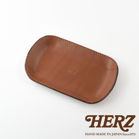 職人手作皮革小物收納盤，淺棕色，以車縫線勾勒邊緣，中央壓印有「HERZ MADE IN JAPAN」字樣。