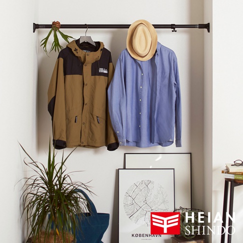 黑色伸縮桿上掛著一件卡其色與黑色拼接的連帽外套，以及一件淺藍色長袖襯衫，襯衫上戴著一頂草編紳士帽。