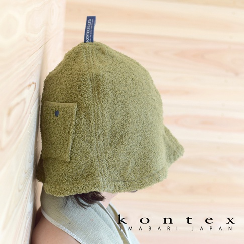 橄欖綠毛巾材質的圓頂桑拿帽，側面有一個帶有鈕扣的方形口袋，頂部有藍色吊牌，整體造型簡潔。