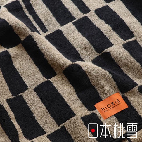 日本桃雪 SOLU 戶外格紋棉柔浴巾，表面有黑色與卡其色交錯的條紋圖案，局部有標籤。