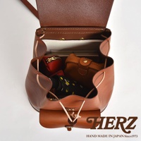 職人手作皮革經典後背包 R-4，以棕色皮革製成，包款內裝有紅色的零錢包、棕色的皮夾、一本筆記本和一把印有黃色花朵圖案的摺疊傘。