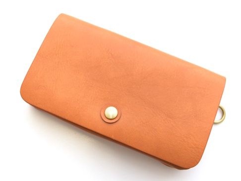 橘棕色皮革製作的長夾，帶有金色按釦和金屬掛環，適合旅行收納護照與機票。