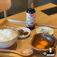 木質托盤上擺放著一碗白飯、兩顆生雞蛋、一瓶標籤為「金笛雞蛋拌飯專用醬油」的醬油瓶、以及兩小碟配菜，分別是醃漬物和豆芽菜。