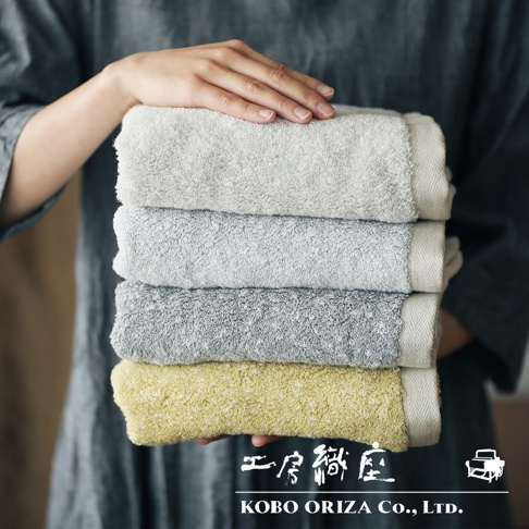 一疊四條SUFFICE 棉麻混紡快乾毛巾，顏色由上至下為淺灰、中灰、深灰和鵝黃。毛巾質地柔軟，邊緣有編織紋理。