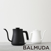 黑色啞光質感的BALMUDA絕美手沖壺，配備細長彎曲壺嘴和人體工學手柄，底部有電源開關。旁邊擺放著一個白色同款手沖壺。