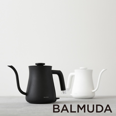 黑色啞光質感的BALMUDA絕美手沖壺，配備細長彎曲壺嘴和人體工學手柄，底部有電源開關。旁邊擺放著一個白色同款手沖壺。