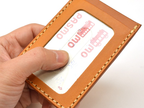職人手作皮革直式票券收納夾，淺棕色牛皮材質，車縫線清晰，內含PASMO交通卡，並由手指展示收納夾的樣式。