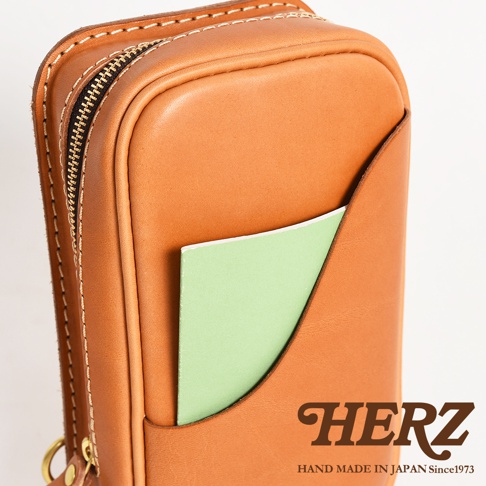 HERZ 品牌手作皮革兩用直立型斜背包，棕色皮革主體，設有拉鍊開口及側邊口袋，露出綠色內頁。