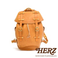 職人手作皮革經典雙扣後背包 R-152，展示為天然棕色皮革，設有兩個可調節的搭扣和抽繩閉合，搭配復古風格的黃銅五金件。