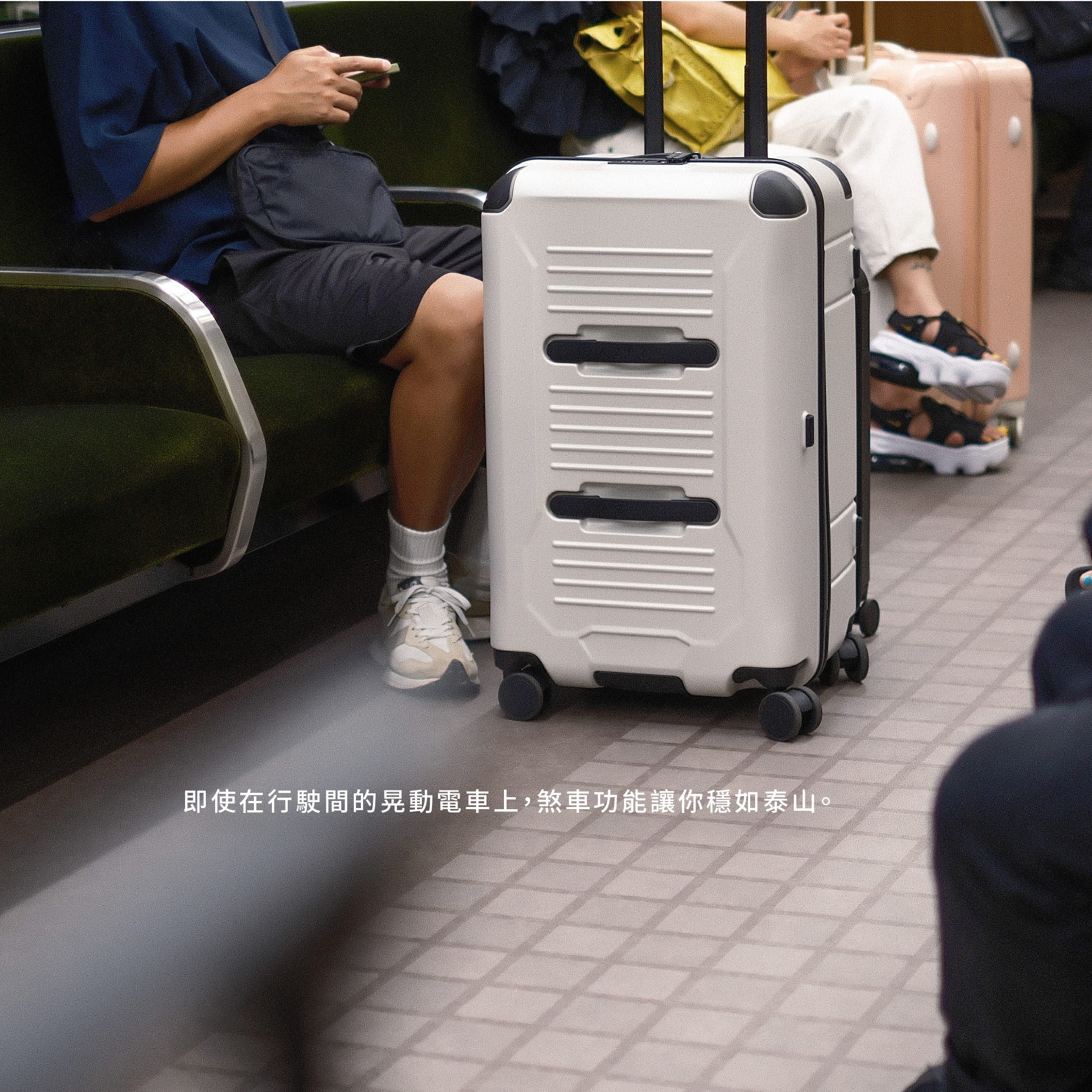 一名乘客坐在電車座椅上，身旁站立著一個白色的 AZPAC 行李箱，圖片下方配有說明文字，強調即便在行駛中晃動的電車上，行李箱的煞車功能也能確保物品穩如泰山。