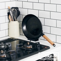 黑色直火專用萬能調理鐵鍋，鍋身為鐵質，附有木質手柄，置於黑色鍋架上，旁邊有白色陶瓷鍋具收納筒，筒內裝有打蛋器、鍋鏟等廚房用具。