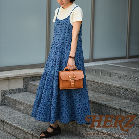 一位女士手持一個棕色皮革迷你單肩包，包上有銀色金屬扣和提把。