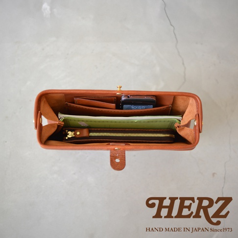 職人手作的棕色皮革Organ手拿包，內部整齊擺放著手機、卡夾、筆記本和拉鍊皮夾。