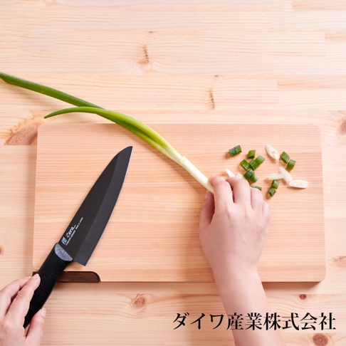 日本製超薄檜木砧板，淺木色，紋理清晰，上面放著一叢青蔥，一隻手正將青蔥切成段，旁邊有一把黑色刀柄的黑色陶瓷刀。