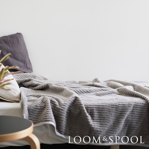 一件灰色立體直紋純棉微厚單人毯，鋪設在床上，搭配深灰色枕頭和白色床單。