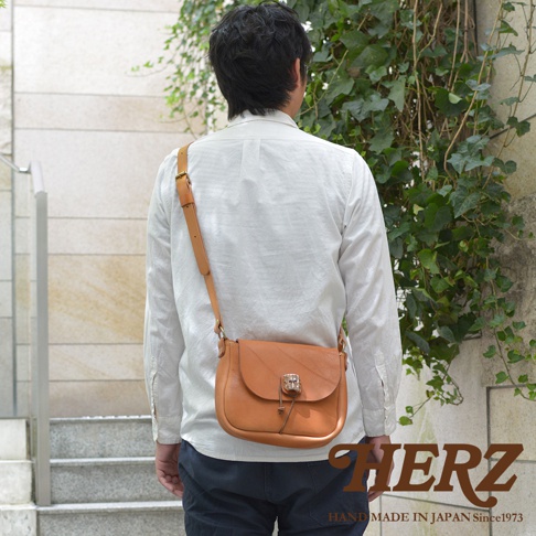 淺棕色皮革製成的職人手作鹿角扣繩肩背包，附有可調節肩帶，由男性側身背於肩上。