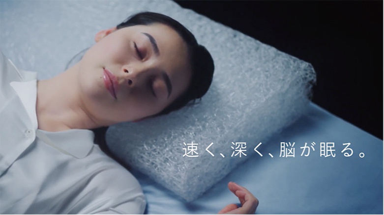 一位女性仰躺在枕頭上，枕頭為白色，表面有細密的紋理，類似泡泡紙。她身穿白色襯衫，臉部朝左，閉眼休息。