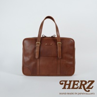 棕色皮革製成的公事包，可肩背或手提，設有兩個提把、兩個可調節的皮帶扣和一個前袋。