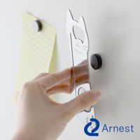 銀色金屬材質的貓咪造型開罐器，帶有貓咪臉部線條雕刻，可吸附在牆面，旁邊有一張黃色條紋紙和黑色磁鐵。