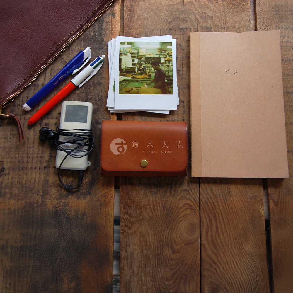 一個棕色皮革製的拉鍊式小物收納袋，上面印有「鈴木太太 SUZUKI SHOP」的日文和英文標誌。