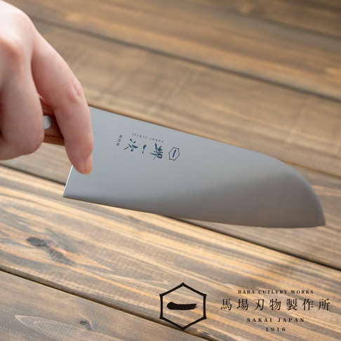 一隻手握著一把不鏽鋼三德刀，刀身上有「堺一次」和「sakai ichiji」的字樣。