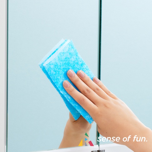 手持藍色、帶有紋理的兩用清潔巾，正在擦拭鏡面。