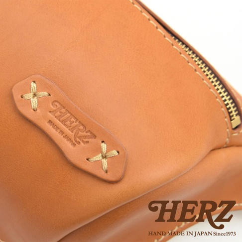 職人手作皮革輕便斜背包 F-5，展示淺棕色皮革材質，有品牌烙印與縫線細節，配有金色拉鍊。