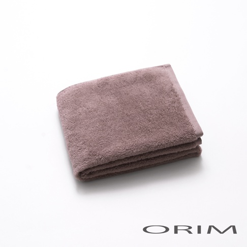 一條對折的淡紫色毛巾，材質柔軟，表面有細緻絨毛，邊緣有縫線。