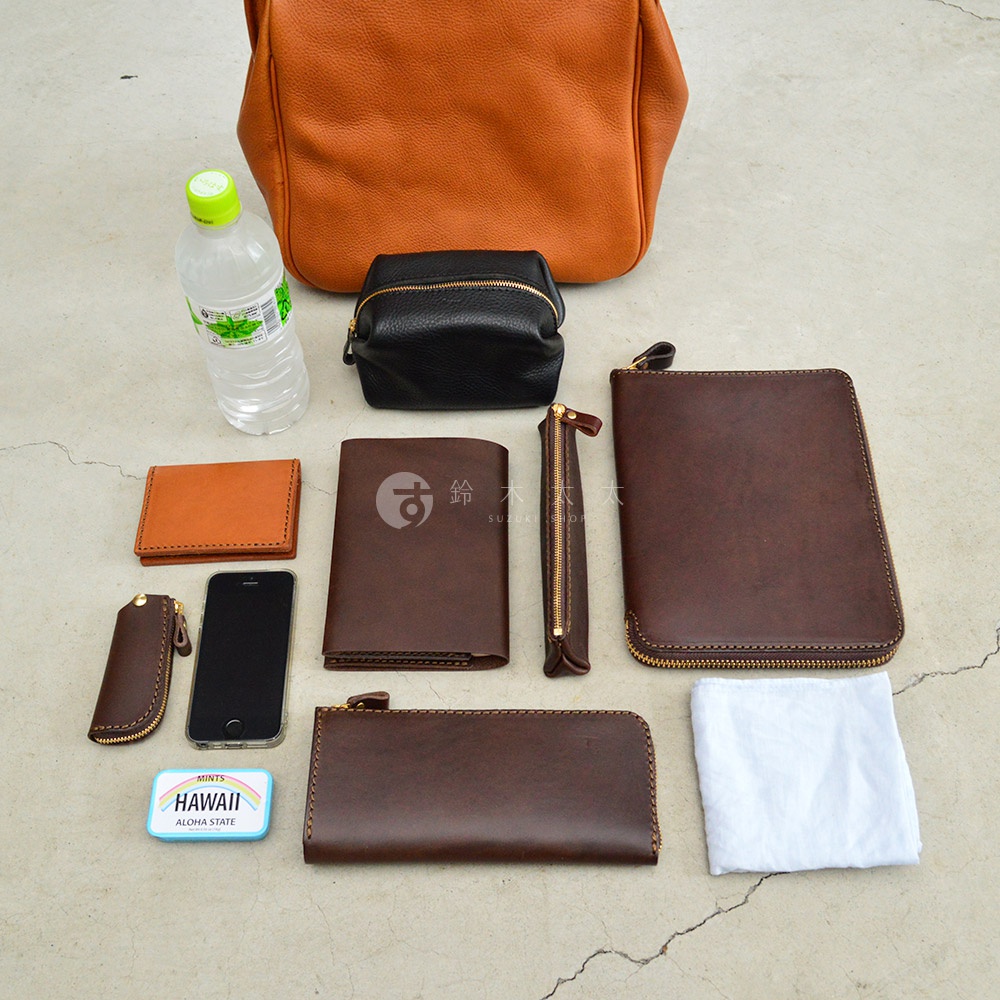展示職人手作皮革Organ兩用方形口金托特包相關配件，包含橘色短夾、黑色化妝包、棕色長夾、手機、鑰匙包、筆袋、收納包及白色布料。