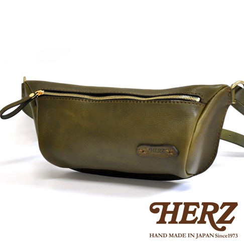 橄欖綠皮革製成的輕便斜背包，具有金色拉鍊和品牌標誌。