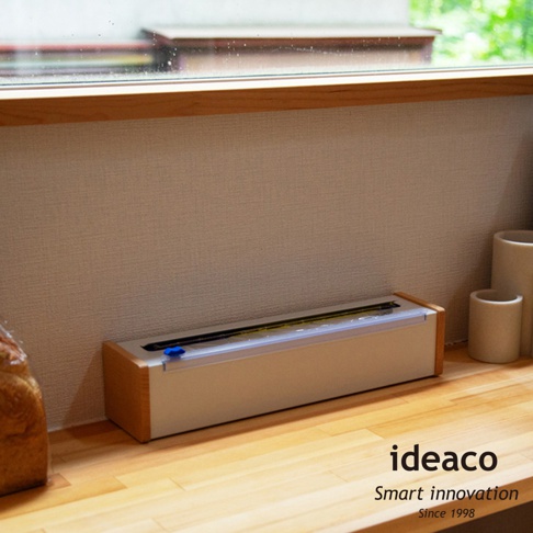 日本製原木鋼製保鮮膜切割器，主體為米白色，搭配原木邊框，切割刀刃清晰可見，整體簡約實用。