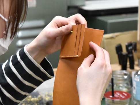 職人手作皮革直式卡片收納雙折短夾，以自然棕色皮革製成，細緻的縫線與金屬釦點綴，展現精湛工藝。