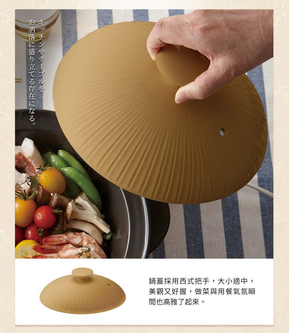 杏色陶土湯鍋鍋蓋，表面帶有放射狀紋路，頂部有圓形把手，鍋蓋上方可見一隻手正在握住把手，下方鍋中盛有燉煮的食材，如蝦、番茄、菇類和豆莢。