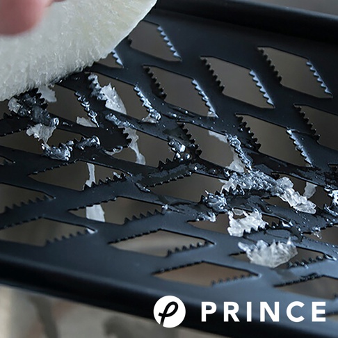 黑色金屬大磨泥器，網格狀孔洞，邊緣有鋸齒狀刀刃，正在磨碎白色食材。