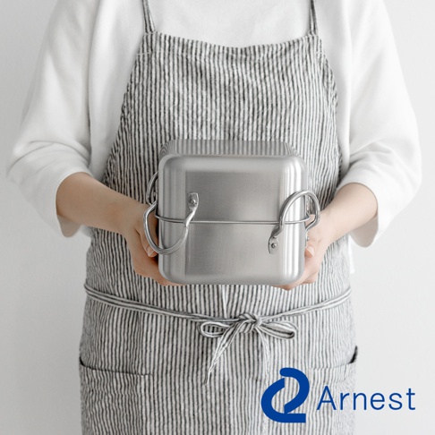 雙手捧著一個銀色不鏽鋼方型炸物鍋組，鍋身有兩個環狀提把，鍋蓋邊緣有一圈金屬束帶。