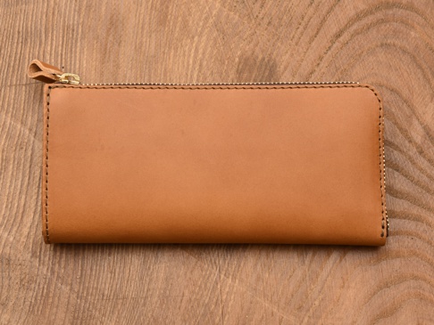 棕色皮革製的L型長夾，表面光滑，兩側有拉鍊設計，左側拉鍊頭配有皮革拉環，整體展現簡約風格。