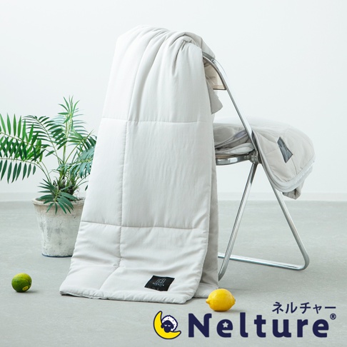 淺灰色五層散熱涼感單人被，表面為格紋縫線，右下角有黑色品牌標籤。被子搭在金屬椅背上，一旁有綠色盆栽和兩個檸檬。